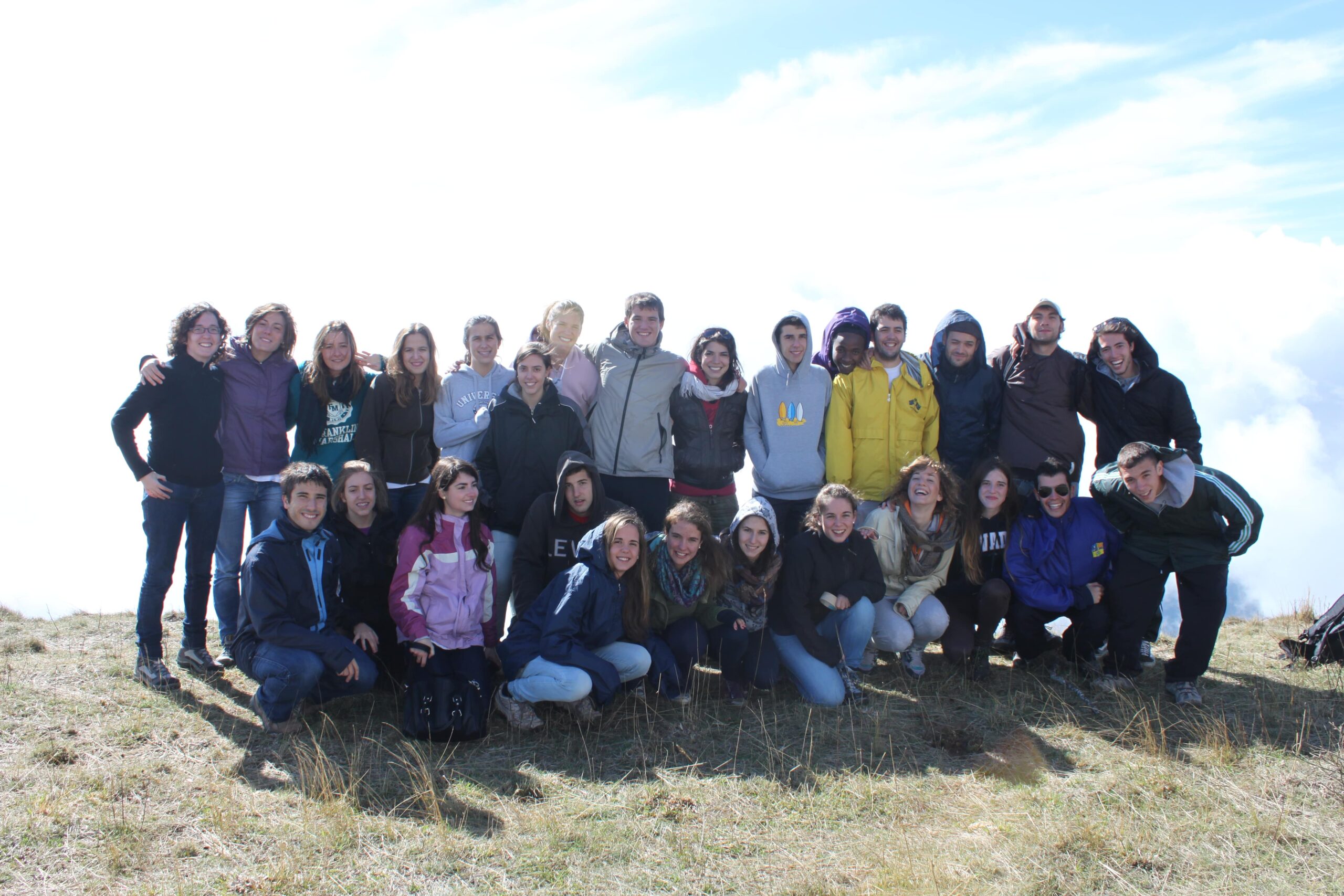 Un grupo numeroso de amigos con Marcos en lo alto de una montaña, sobre un mar de nubes